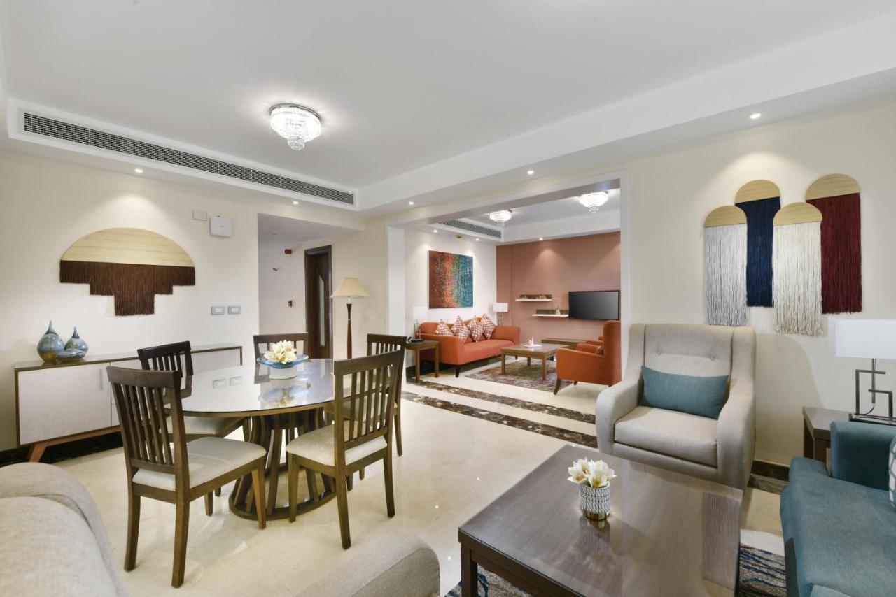 톨립 리조트 엘 갈라라 마제스틱 아인 수크나 외부 사진 The photo shows a modern living room space that is elegantly designed. It features a seating area with a comfortable sofa and armchairs, complemented by a decorative coffee table. There is a dining table with several wooden chairs, providing a cozy a