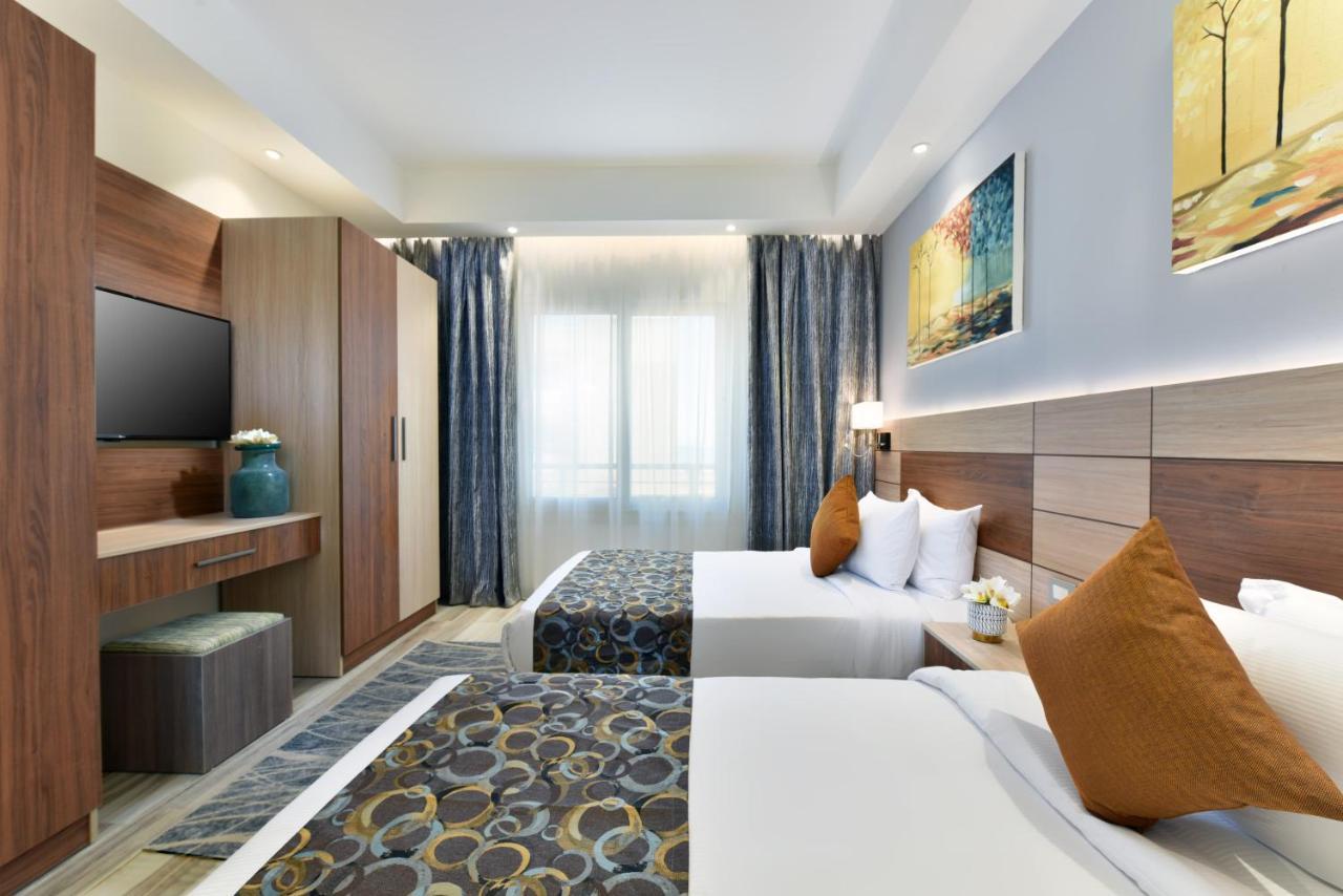톨립 리조트 엘 갈라라 마제스틱 아인 수크나 외부 사진 The photo shows a well-decorated hotel room with two twin beds, each adorned with white linens and brown decorative pillows. There's a modern wooden wardrobe in the corner, alongside a flat-screen TV mounted on the wall. The room features large windo