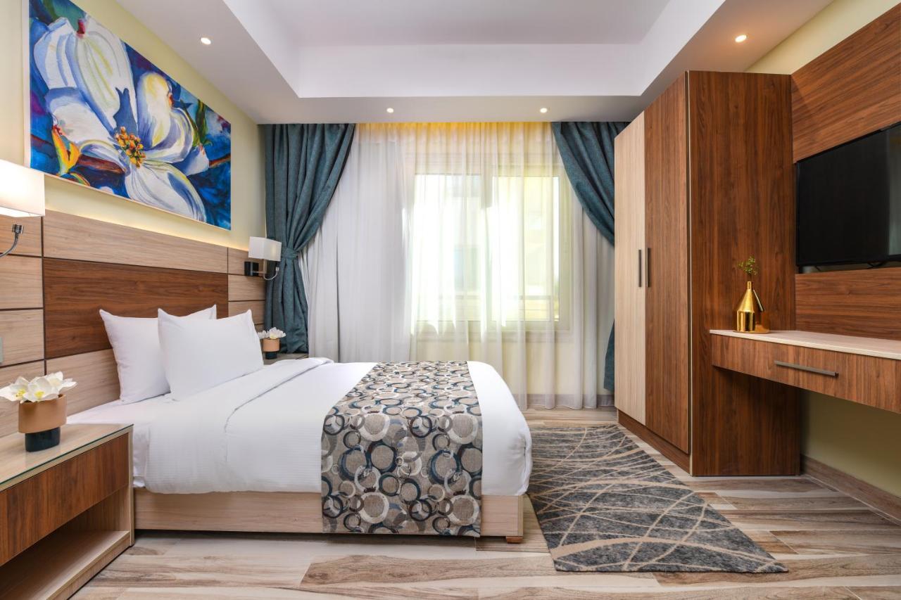 톨립 리조트 엘 갈라라 마제스틱 아인 수크나 외부 사진 The photo shows a well-designed hotel room. It features a comfortable bed with a decorative bedspread and two pillows. There are soft curtains framing a window that lets in natural light. On one side, there is a colorful piece of artwork hanging on t