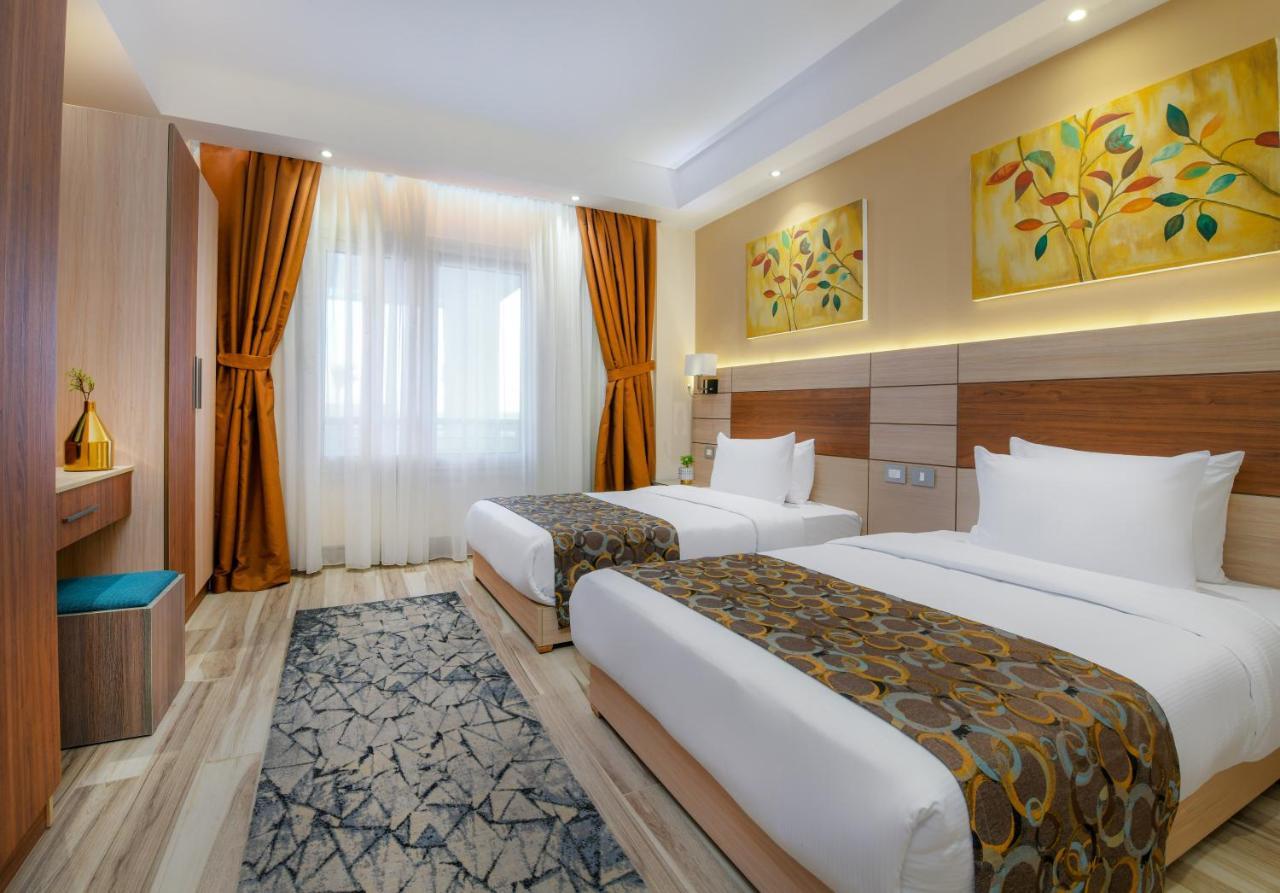 톨립 리조트 엘 갈라라 마제스틱 아인 수크나 외부 사진 The photo shows a modern hotel room with two single beds, each covered with white linens and decorative brown bed throws. The walls are painted in warm colors, and there are two pieces of artwork featuring floral and leaf designs above the beds. The 