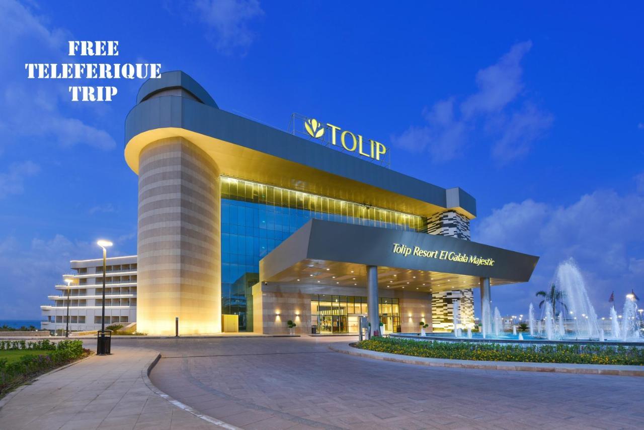 톨립 리조트 엘 갈라라 마제스틱 아인 수크나 외부 사진 The photo shows a modern hotel building named "Tolip Resort & Spa," featuring a sleek architectural design with large glass windows. The hotel is illuminated against a twilight sky, showcasing its prominent signage. In the foreground, there is a well