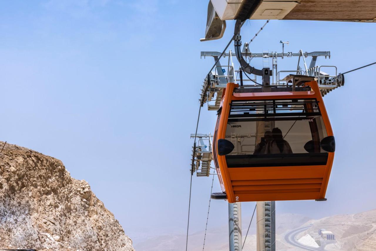 톨립 리조트 엘 갈라라 마제스틱 아인 수크나 외부 사진 The photo shows an orange gondola or cable car hanging on a cable system. The gondola appears to be suspended in the air above a rocky landscape, with a clear sky in the background. There are supporting cables and structures visible, indicating that 