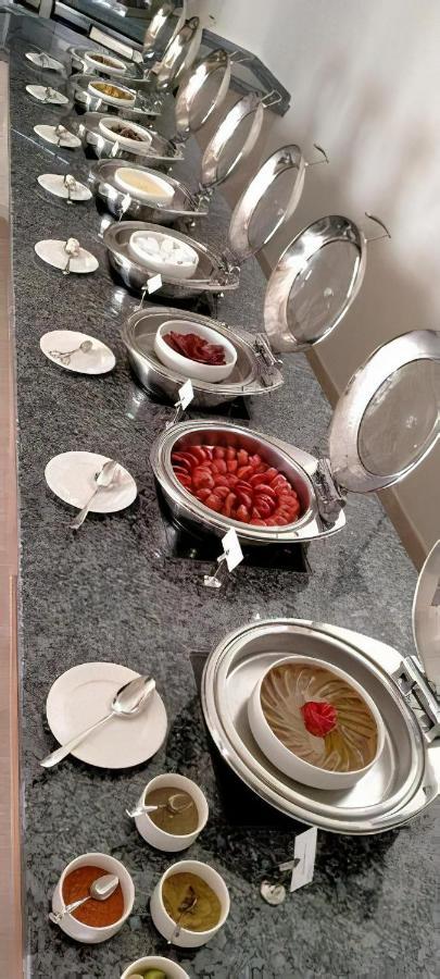톨립 리조트 엘 갈라라 마제스틱 아인 수크나 외부 사진 The photo shows a buffet setup featuring multiple metal serving trays on a dark granite countertop. One tray contains circular slices of food, possibly sausages or a similar dish, while another bowl holds what appears to be red food items, though it'