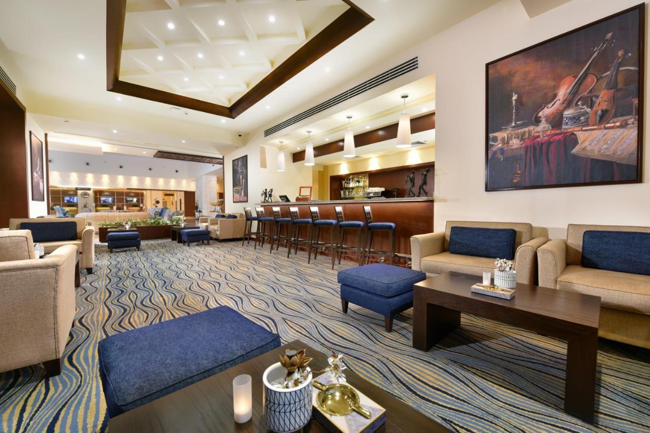 톨립 리조트 엘 갈라라 마제스틱 아인 수크나 외부 사진 The photo depicts a modern, inviting lobby or lounge area. It features a cozy seating arrangement with light-colored sofas and deep blue accent chairs. In the center, there is a low wooden coffee table with decorative items, including a candle and sm
