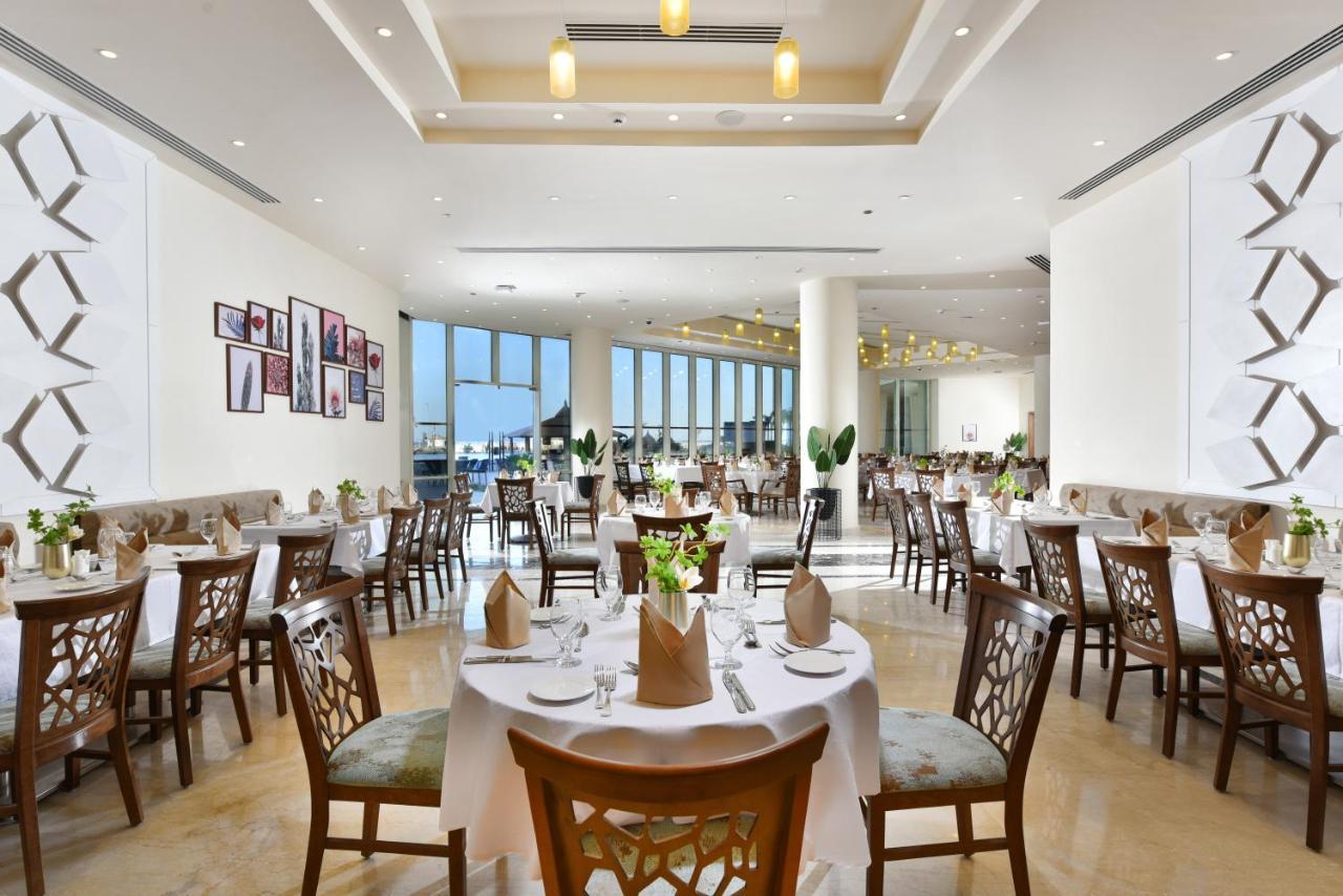 톨립 리조트 엘 갈라라 마제스틱 아인 수크나 외부 사진 The photo displays a spacious and elegantly designed restaurant interior. It features numerous tables set for dining, with white tablecloths, neatly folded napkins, and decorative centerpieces of flowers. The seating consists of wooden chairs that co