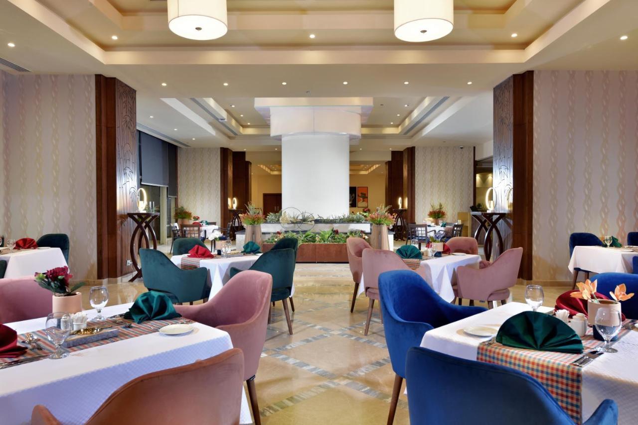 톨립 리조트 엘 갈라라 마제스틱 아인 수크나 외부 사진 The photo shows a spacious and elegantly designed restaurant interior. The layout includes several round tables dressed in white tablecloths, each set with decorative plates, cutlery, and colorful napkins. The chairs are upholstered in a variety of c